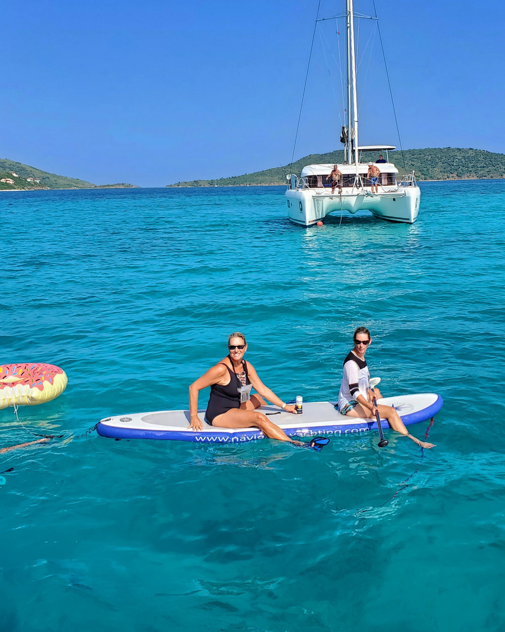 Two guests on a paddleboard near an anchored catamaran