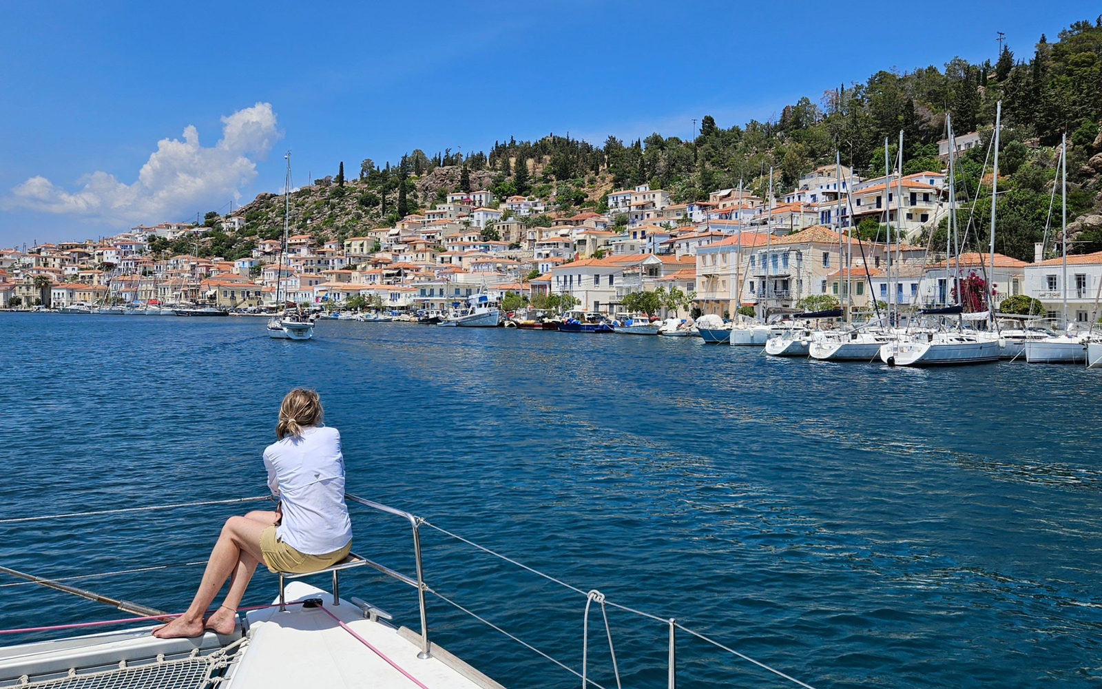 Guest on the bow of a sailboat looking at a Greek harbor town