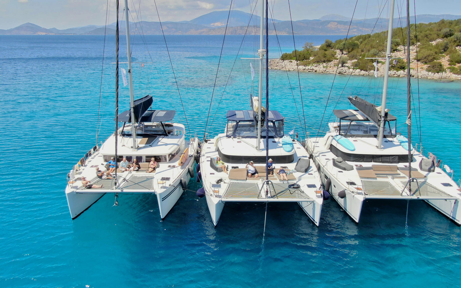 Three catamarans anchored in clear turquoise water in Greece